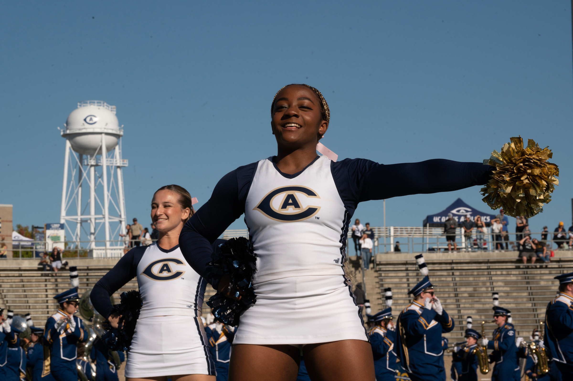 Image of UC Davis cheerleaders at the 2025 homecoming football came with the newly restored Touchdown Tower in the background.