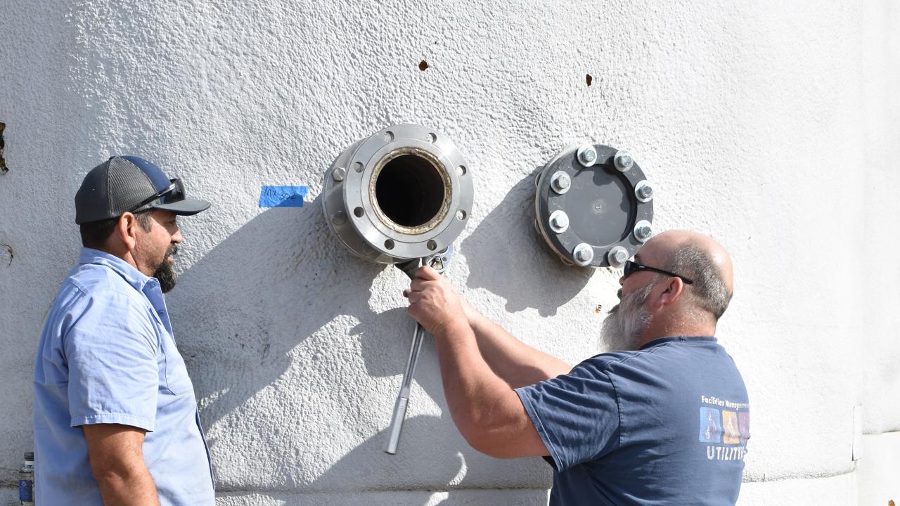 Utilities staff Joe Adamson and Horacio Mendoza from the Cooling & Heating Central Plant (CHCP), install connections on one of the large tanks needed to remove the ammonia from digestate at the READ facility.