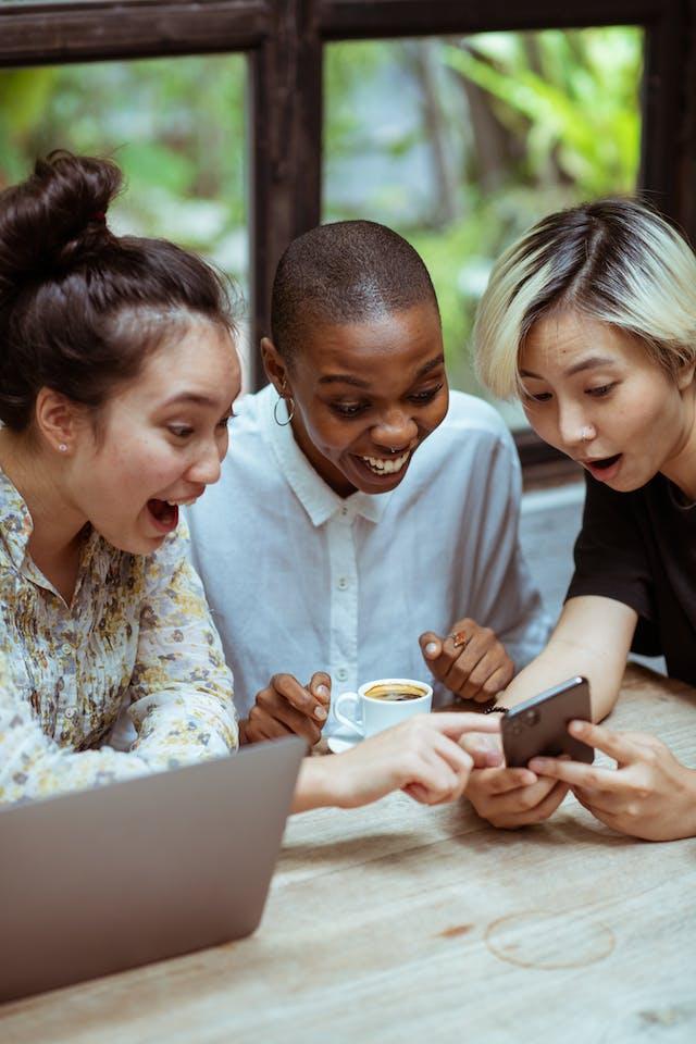 Image of three young people looking at a phone and laughing.