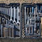 Open black tool case on pavement with organized wrenches, sockets, and screwdrivers