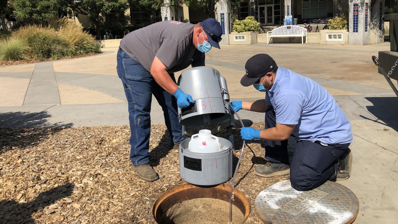 Utilities staff, Cody Hays and Scott Wedding, install an auto sampler that will collect sewage water samples for use in coronavirus testing. Two employees install a coronavirus auto sampler.
