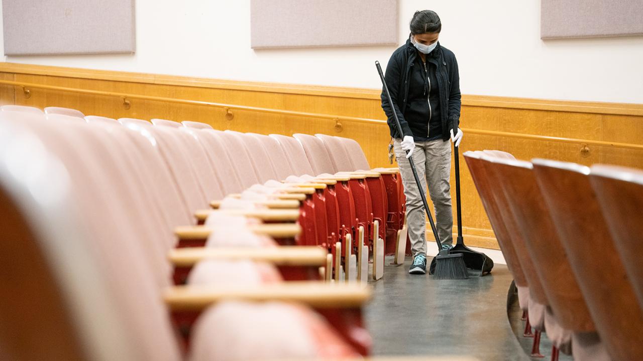 Custodian sweeps between rows of seats at a lecture hall